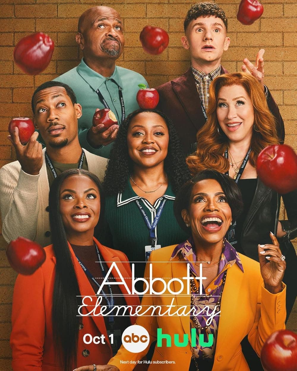 Elenco de Abbott Elementary sorrindo sob maçãs vermelhas caindo contra parede de tijolos.